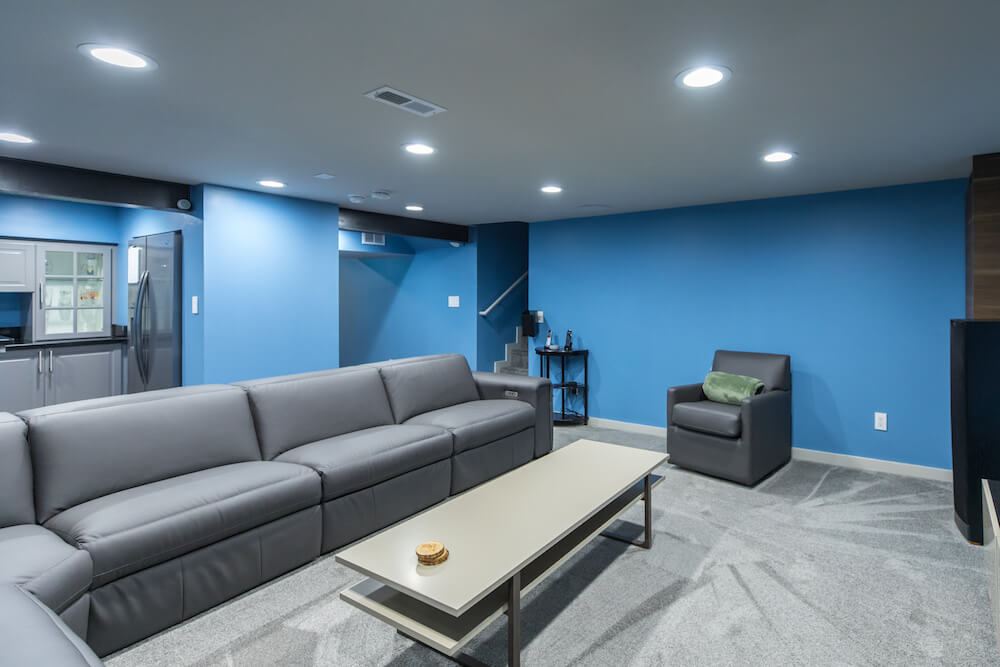 Blue wall with gray carpet in the entertainment room with white false ceiling and recessed lights after renovation