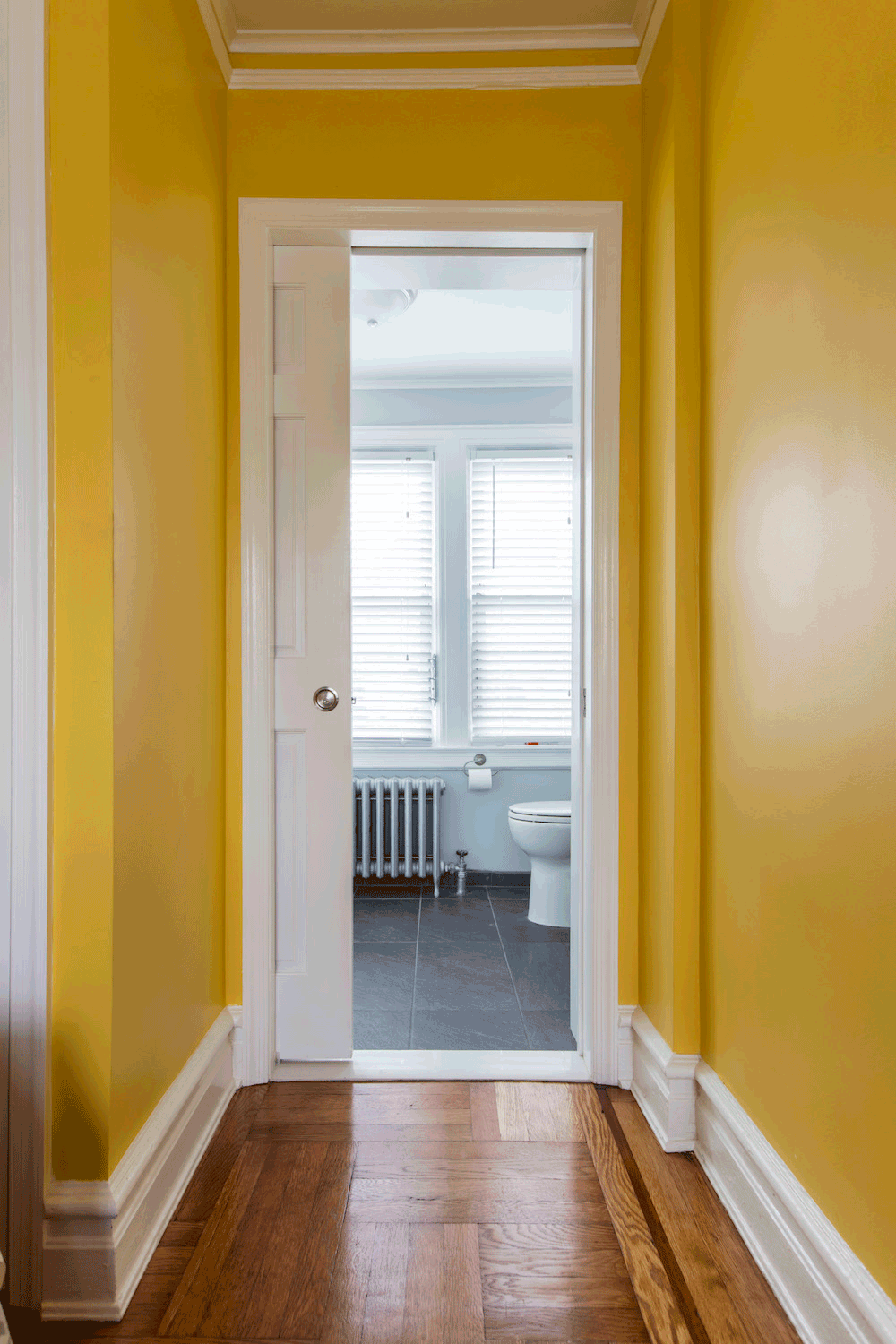 hallway with bright yellow walls and white shoe molding and hardwood floors and white doors to bathroom after renovation