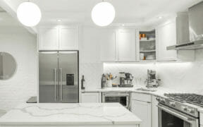 white kitchen cabinets and white backsplash and stainless steel appliances and island with ball pendant lights after renovation