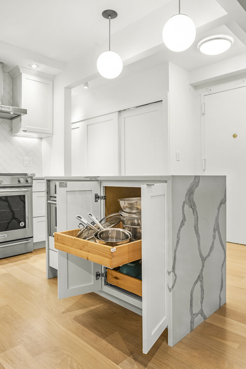 kitchen with white cabinets and stainless steel appliances and hardwood floor and waterfall marble island with pull out drawers inside cabinets and pendant lights after renovation