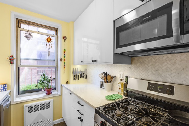 white kitchen cabinets with black handles and off-white countertop and yellow walls and herringbone backsplash and stainless steel appliances after renovation