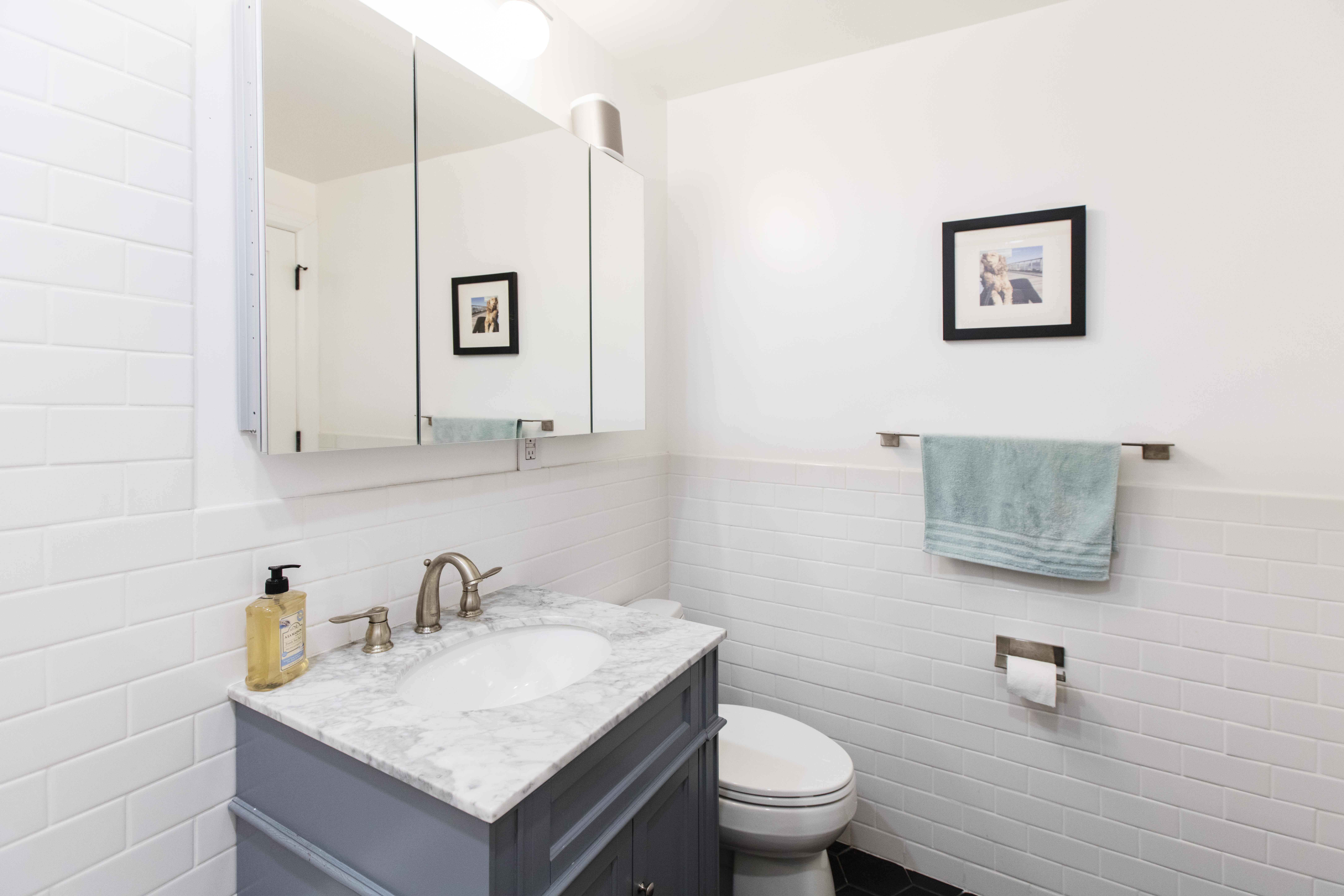 A gray marble-top vanity, mirrored cabinet, white subway tile, and black hex flooring refresh this compact Financial District bathroom.