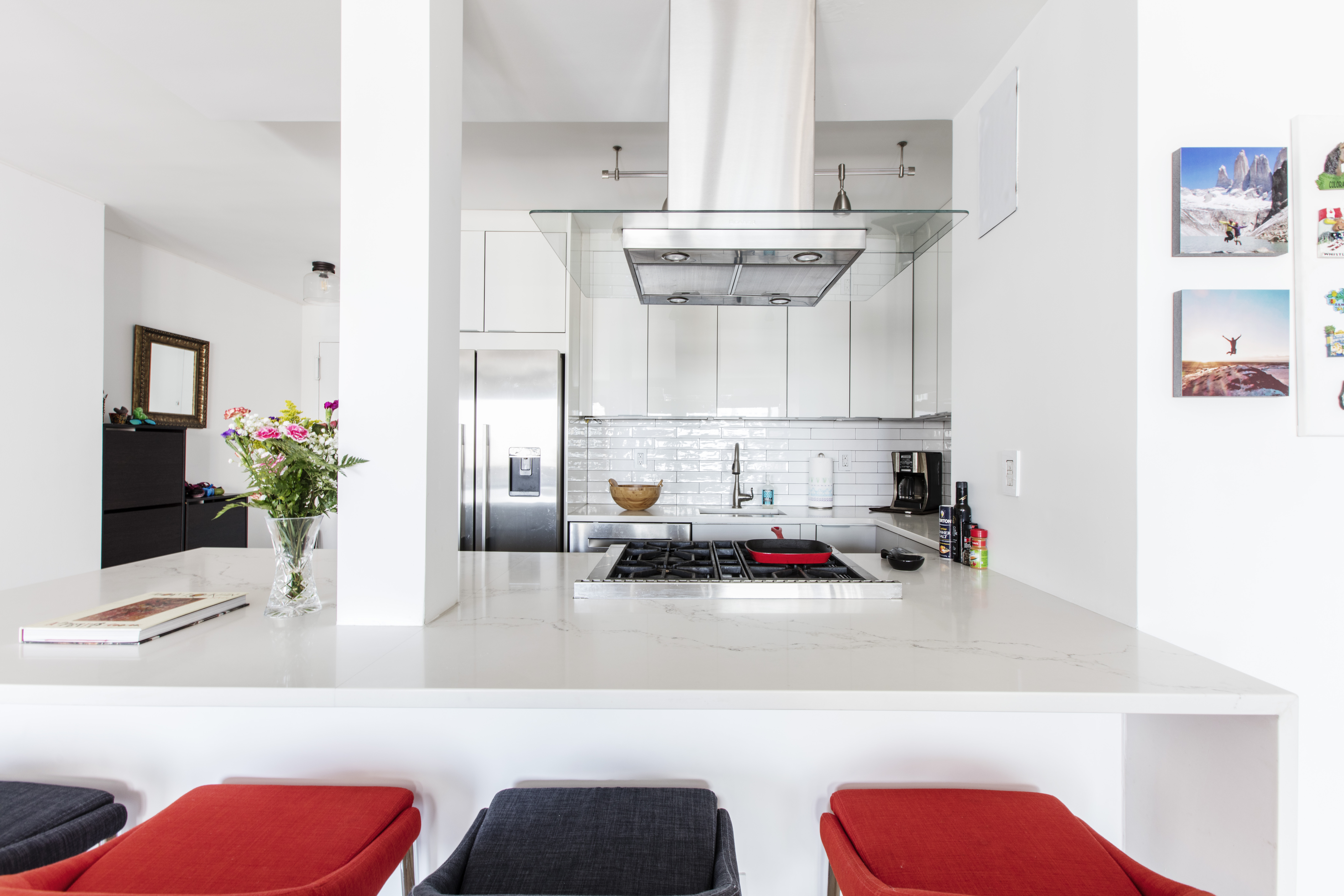 An open white kitchen in New York City features quartz counters, glossy cabinetry, stainless appliances, and a peninsula with built-in cooking space.