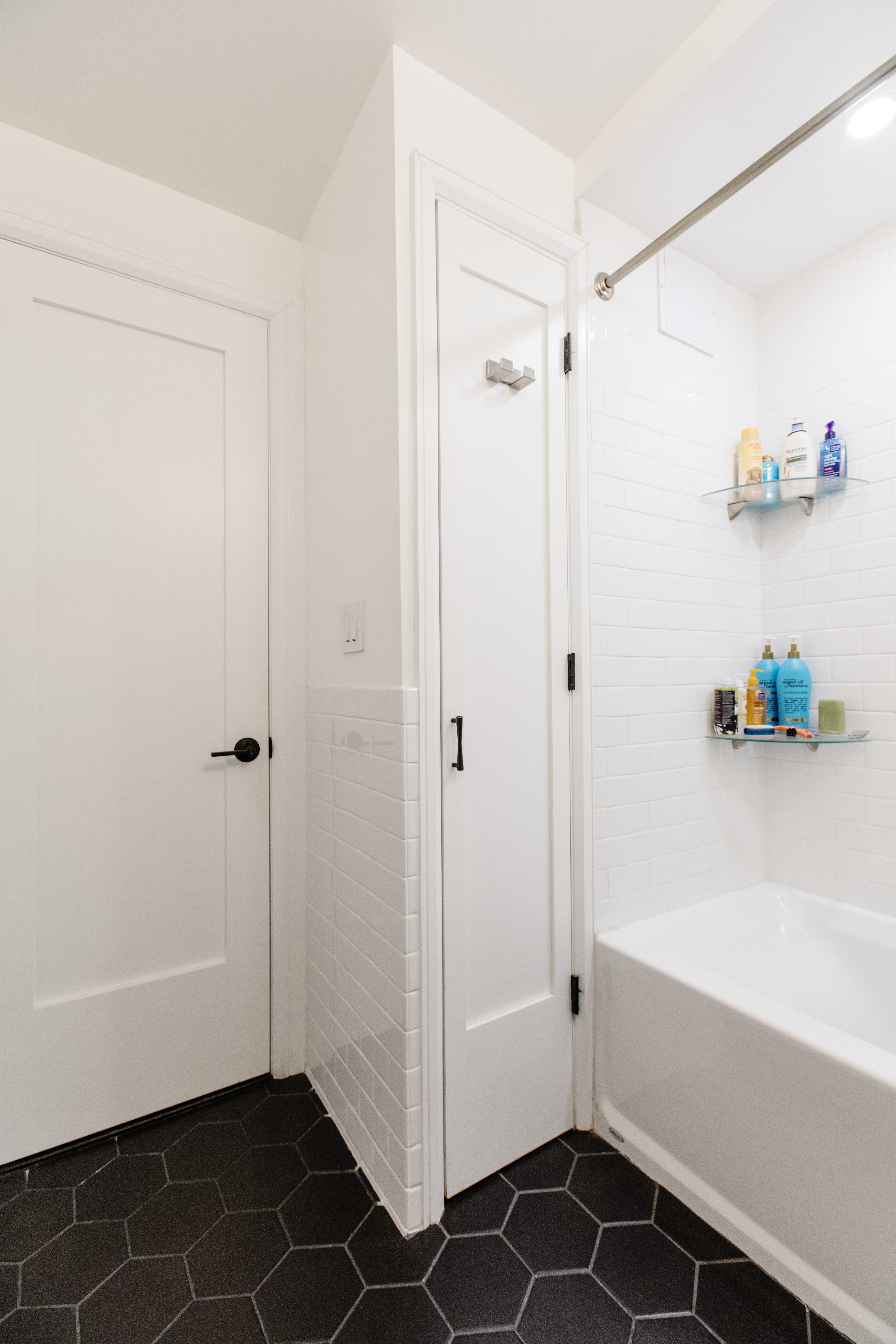 White subway tile, black hex flooring, built-in storage, and a tub-shower combination update this compact New York City bathroom.