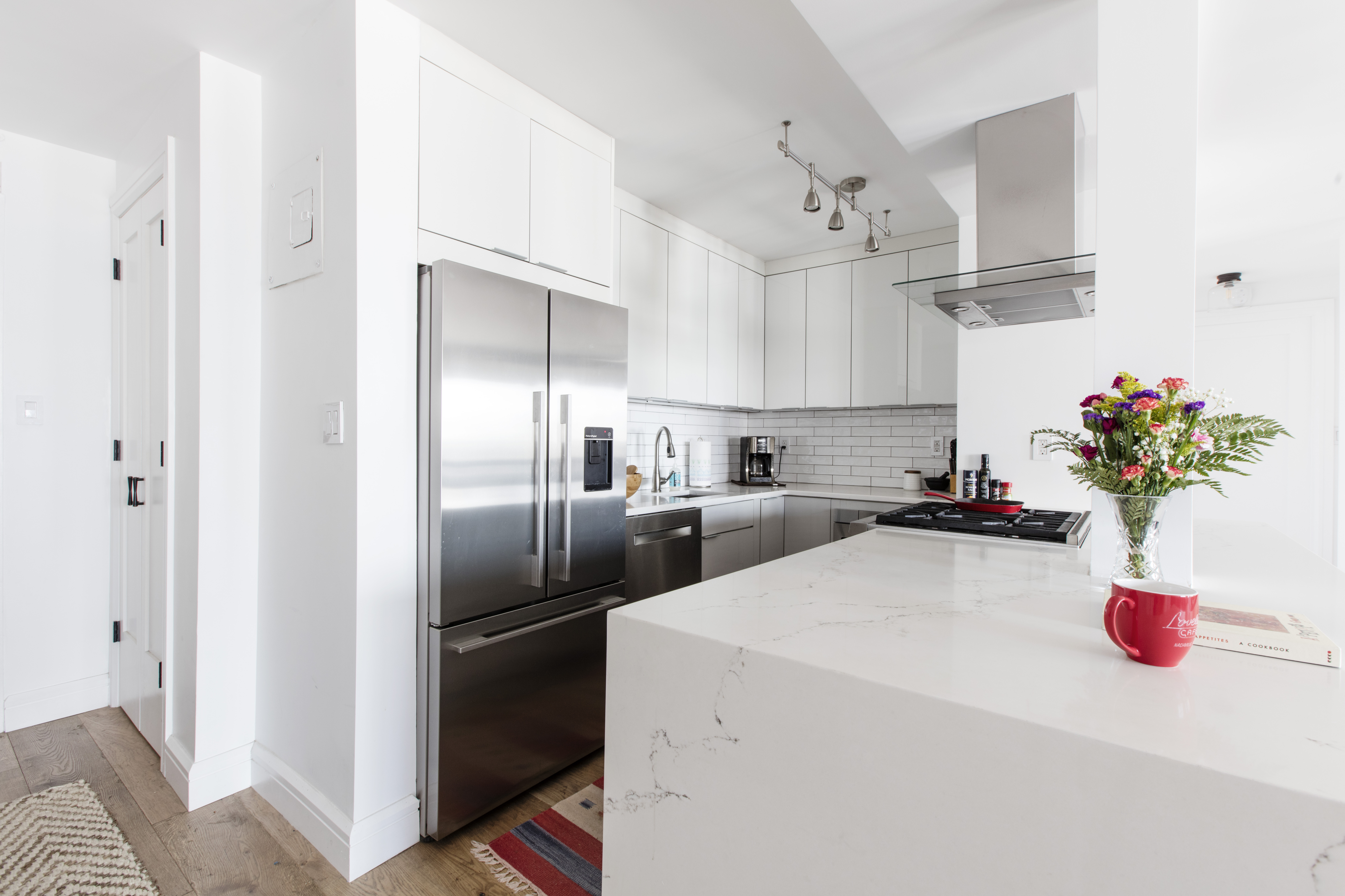 A renovated New York City kitchen pairs wide oak flooring with white cabinetry, quartz counters, subway tile, and stainless steel appliances.