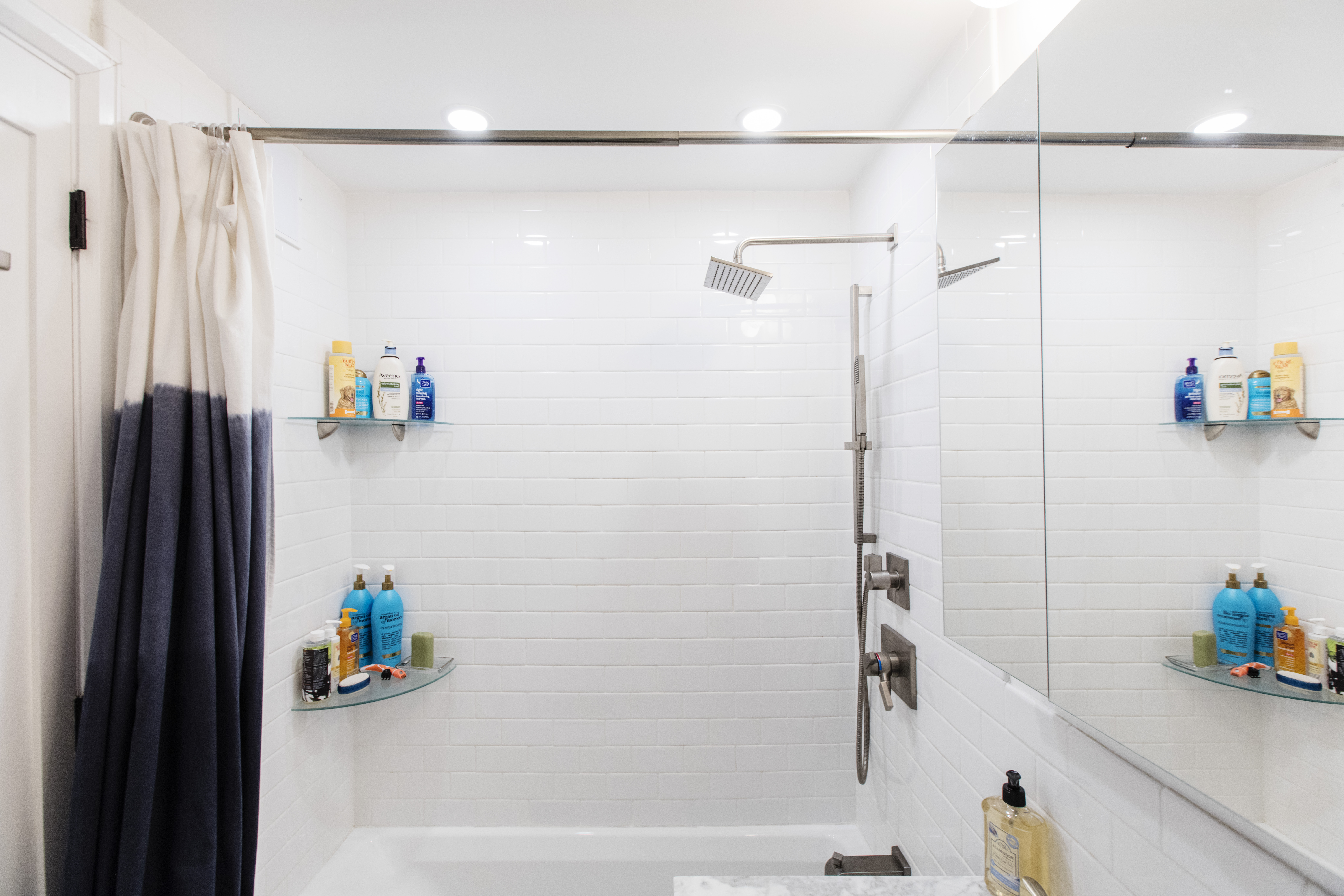 White subway tile surrounds the tub and shower, paired with streamlined stainless fixtures and glass shelves in this Financial District bathroom.