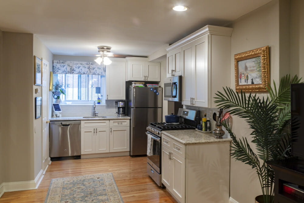 white overhead kitchen cabinets and off-white under counter cabinets and stainless steel appliances and beige walls and hardwood floors and recessed lighting and ceiling fan with light after renovation