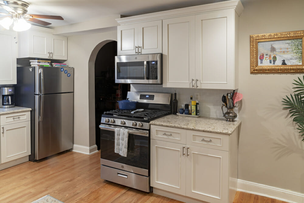 white overhead kitchen cabinets and off-white under counter cabinets and granite countertop and stainless steel appliances and beige walls and hardwood floors and ceiling fan with light after renovation