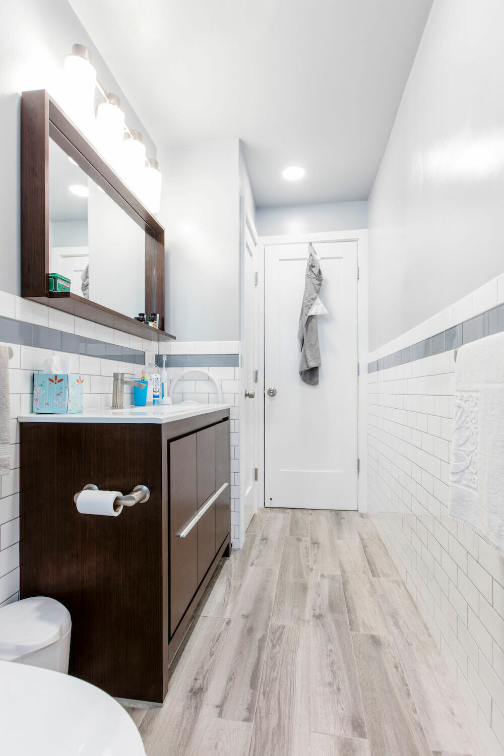 White subway tiles with light blue trim and white sink over brown vanity after renovation