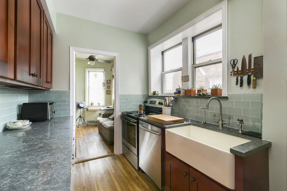 mahogany cabinets and green backsplash and gray countertop and hardwood floors and farmhouse sink with faucets and stainless steel appliances and pastel green wall paint after renovation