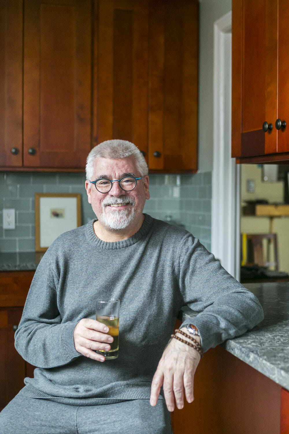 ed sitting in his kitchen with mahogany cabinets and green backsplash and gray countertop after renovation