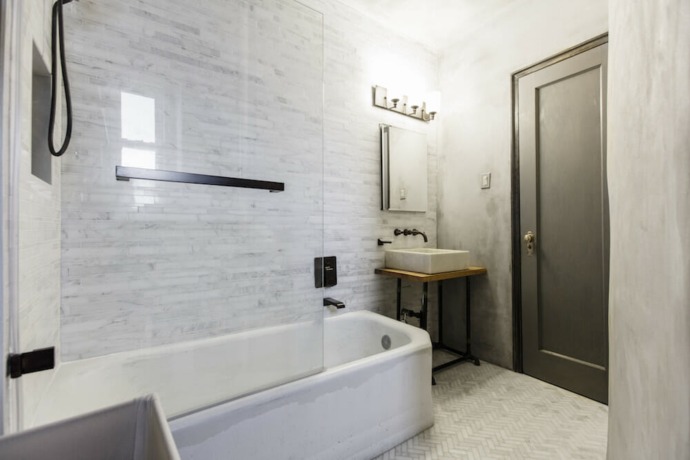 bathroom with light gray tiles on floor and walls and console sink and medicine cabinet with mirror and bathtub with glass wall after renovation