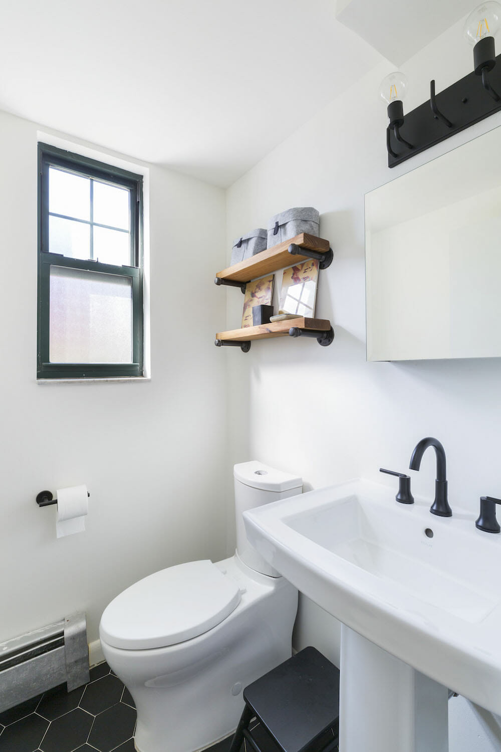 pedastal sink with black faucet and fixtures and wooden shelves above toilet and black hexagon floor tiles and medicine cabinet with mirror after renovation