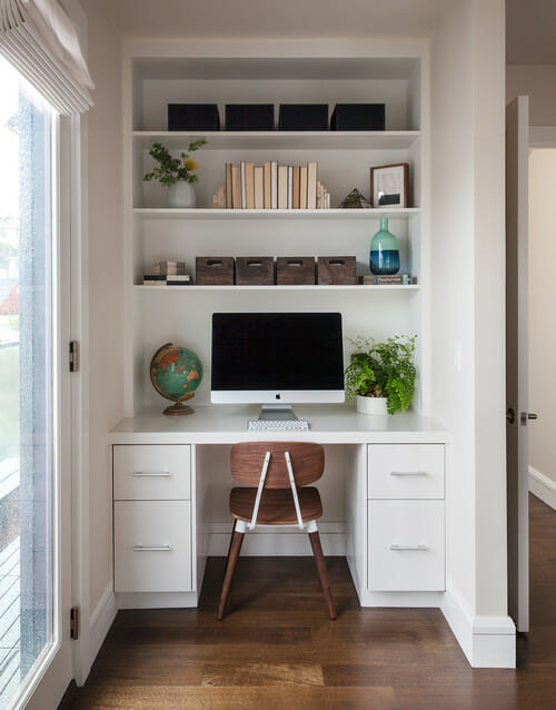 tiny study nook with white desk and drawers with handles and white open shelves after renovation