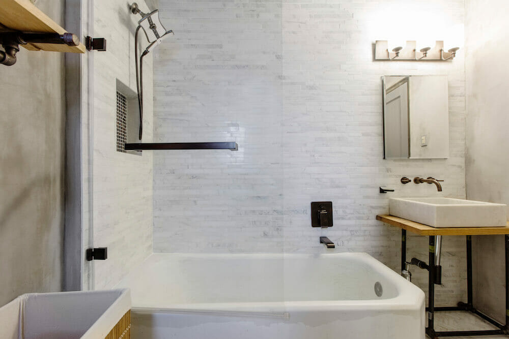 white bathtub and marble sink with wall mounted faucet on white wall tile after renovation