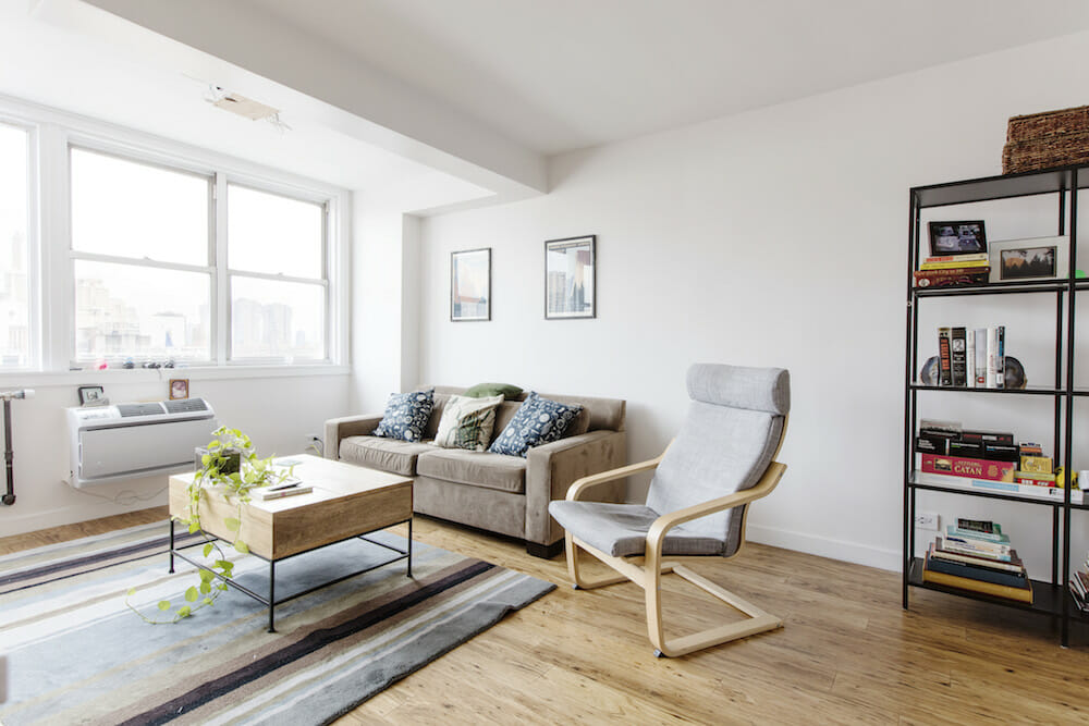 living room with white walls and hardwood floors and wall mounted air conditioner below window after renovation