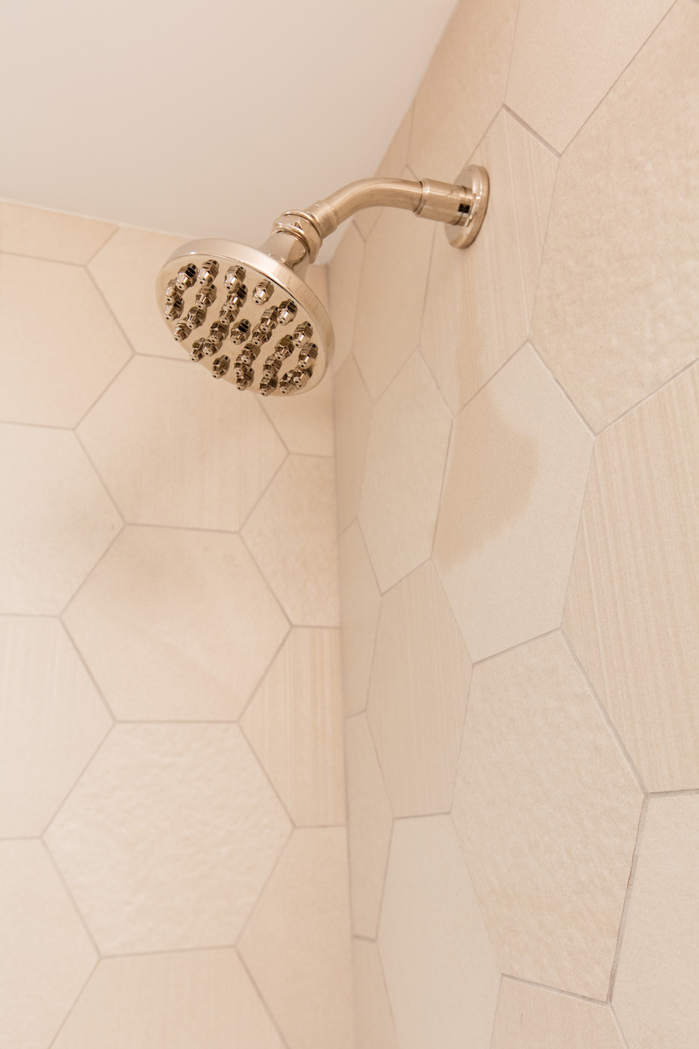 brushed brass shower head on off-white hexagon wall tiles after renovation 