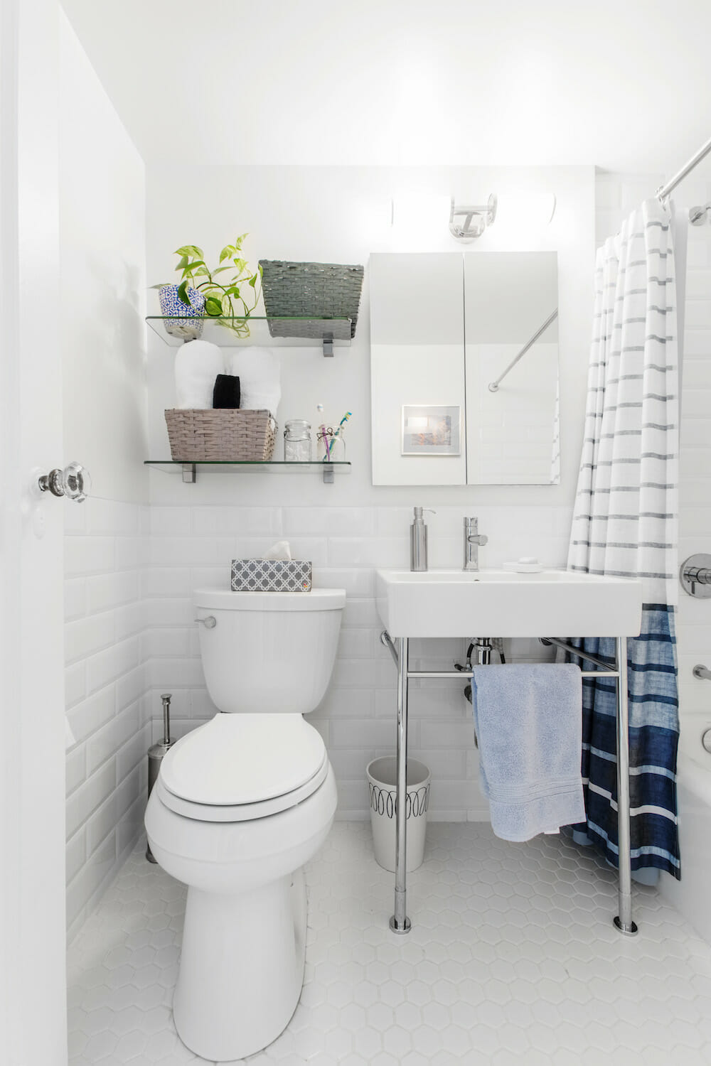 white bathroom with console sink and mirror and white subway tiles on walls and floating glass shelves after renovation