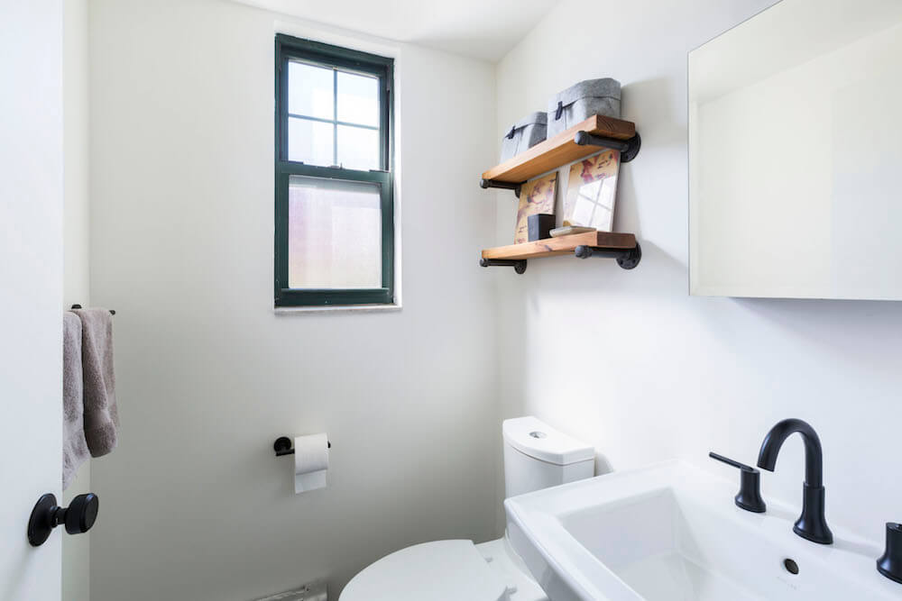 Black double hung window near floating wooden shelves and white farmhouse sink after renovation