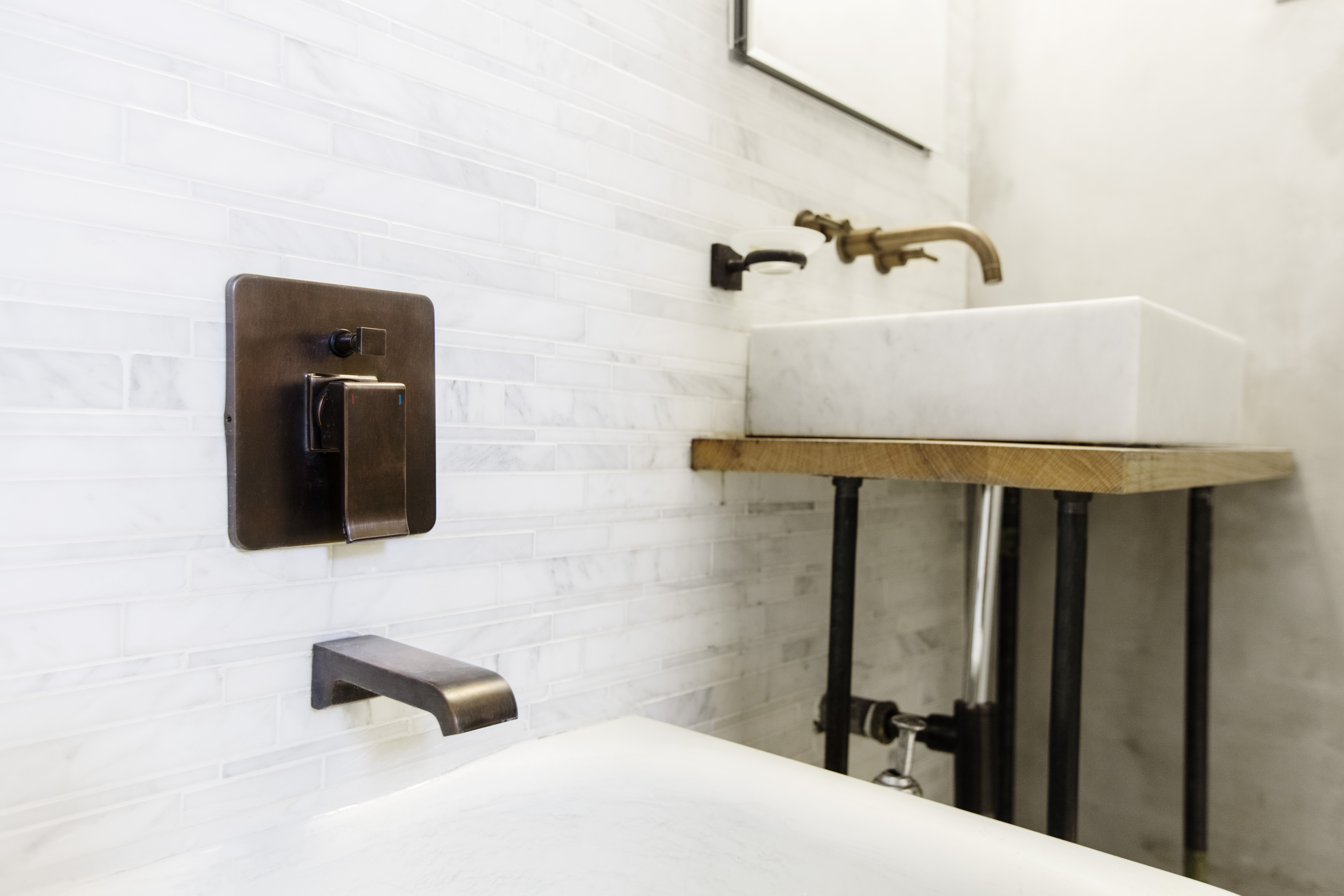 Wabi-sabi bathroom detail in Windsor Terrace with marble wall tile, bronze tub controls, a wall-mounted faucet, vessel sink, and wood vanity surface.