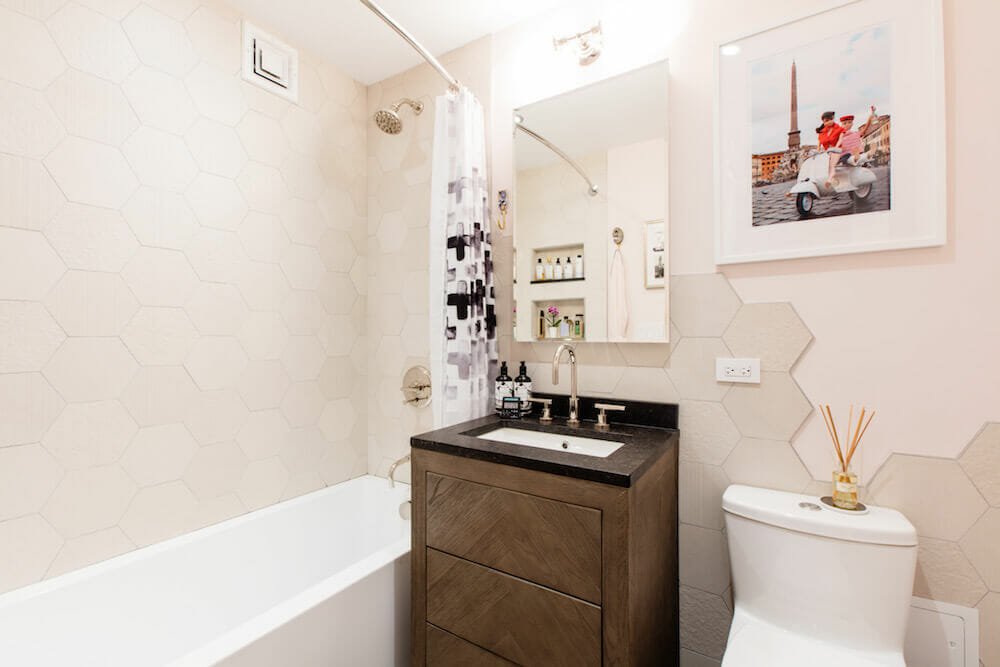 Three drawer herringbone vanity over sink near white bathtub with hexagon tiles on shower wall after renovation