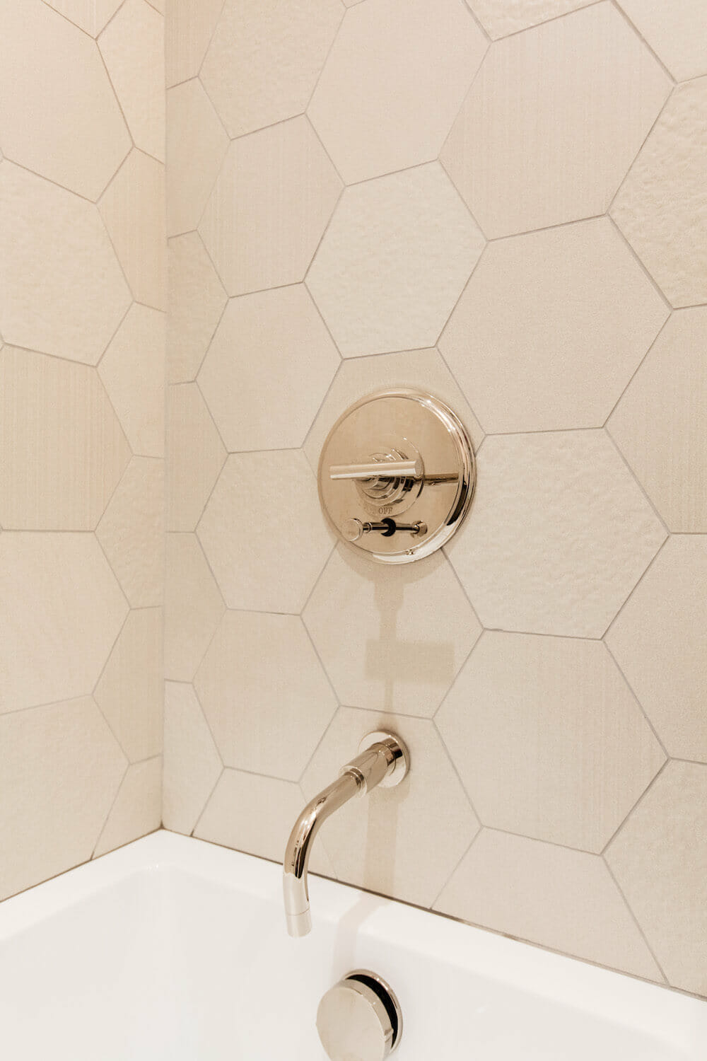 Matte gold bathroom fixtures with hexagon tiles for shower wall and white tub after renovation