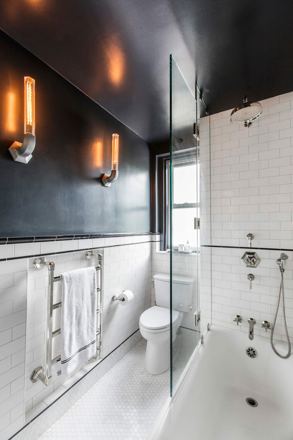Black and white bathroom with shower glass and wall sconces and white bathtub after renovation