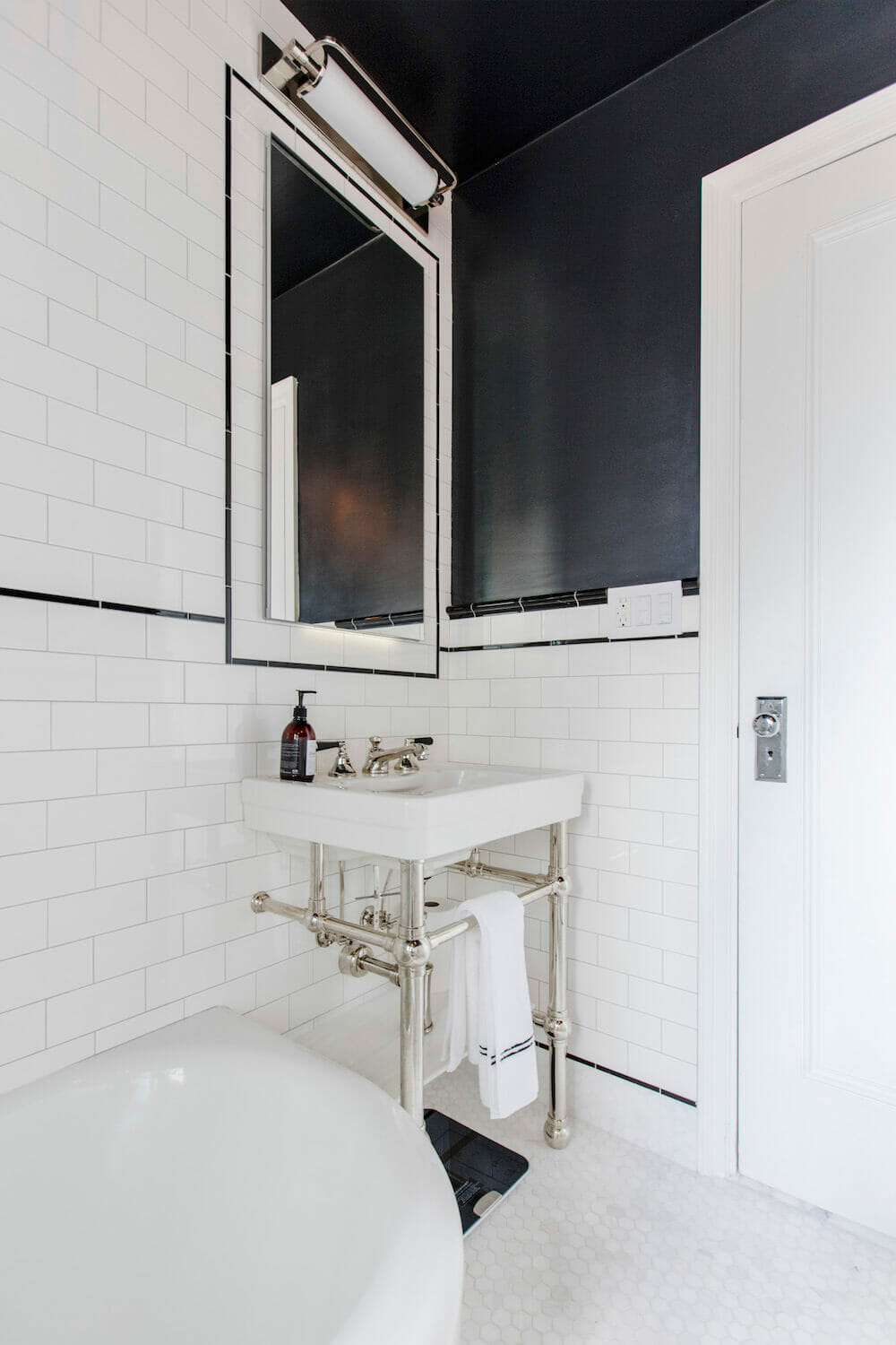 White pedestal sink with console legs in a white and black bathroom with large vanity mirror after renovation