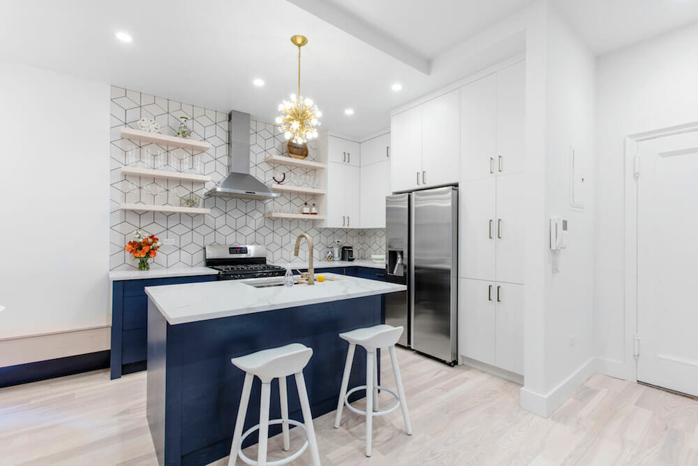 blue kitchen island with white walls and white cabinets along with open shelves on a light wooden flooring after renovation