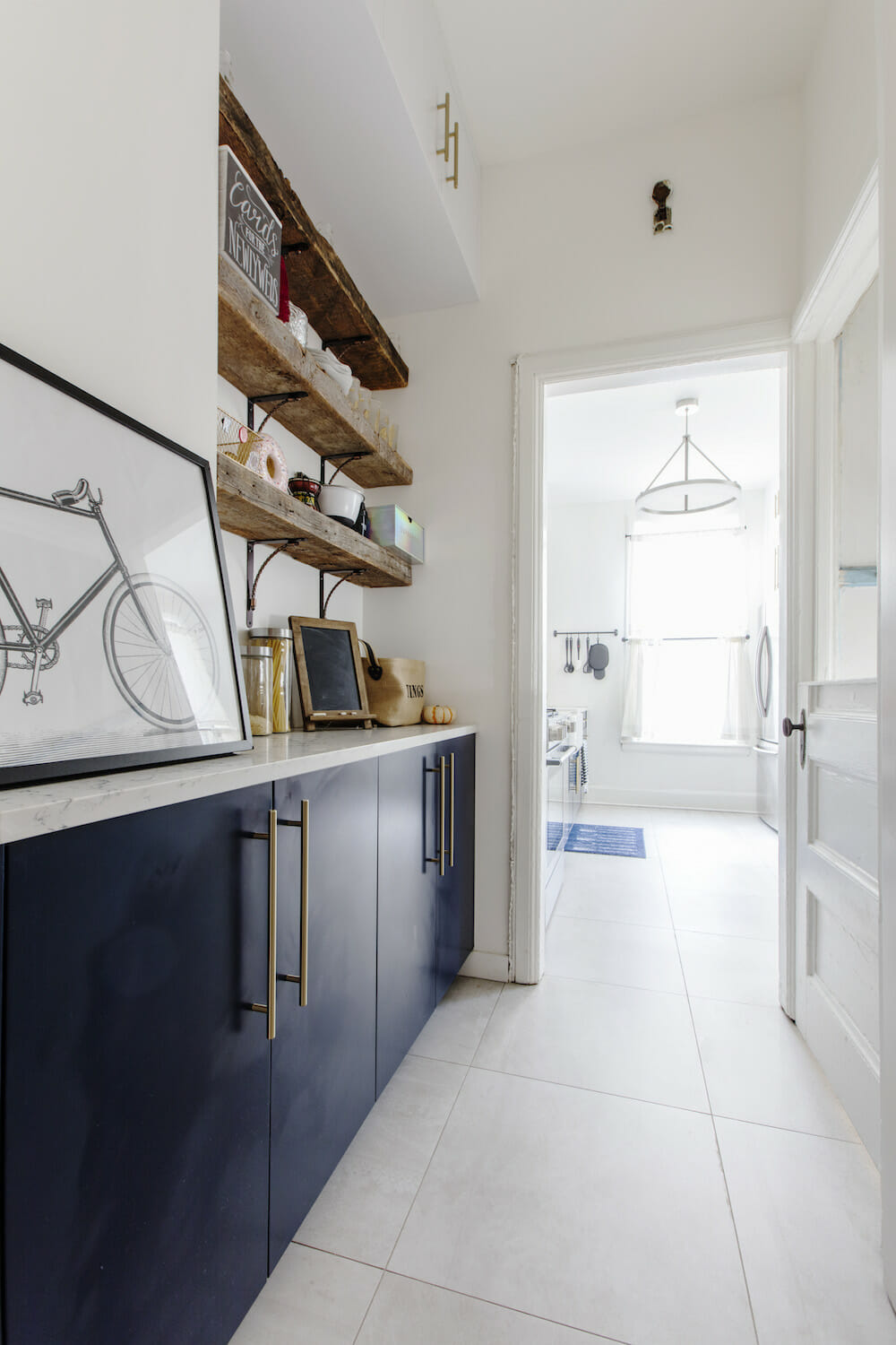 white kitchen countertop with navy blue cabinets and white walls and floating wooden shelves with brackets and white floor tiles after renovation