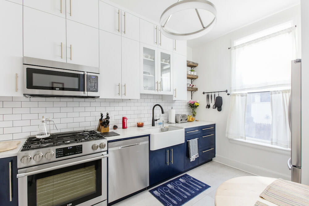 kitchen with white overhead cabinets and white countertop and navy blue cabinets under counter and stainless steel appliances and backsplash with white subway tiles after renovation