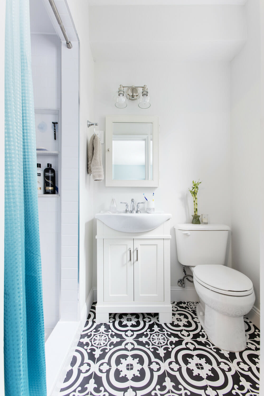 bathroom with white walls and white vanity with medicine cabinet and toilet and black and white patterned floor tiles after renovation