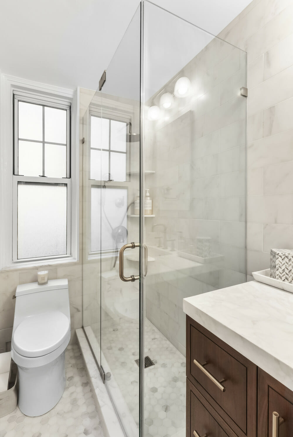 bathroom vanity with marble countertop and toilet below window and walk-in shower with glass wall and door after renovation