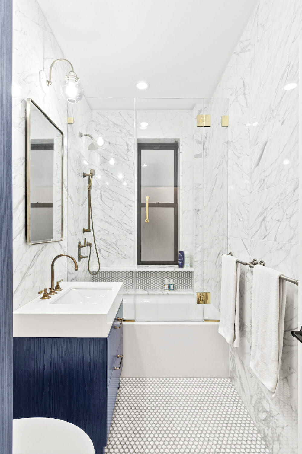 bathroom with blue cabinets, marble tile and gold fixtures