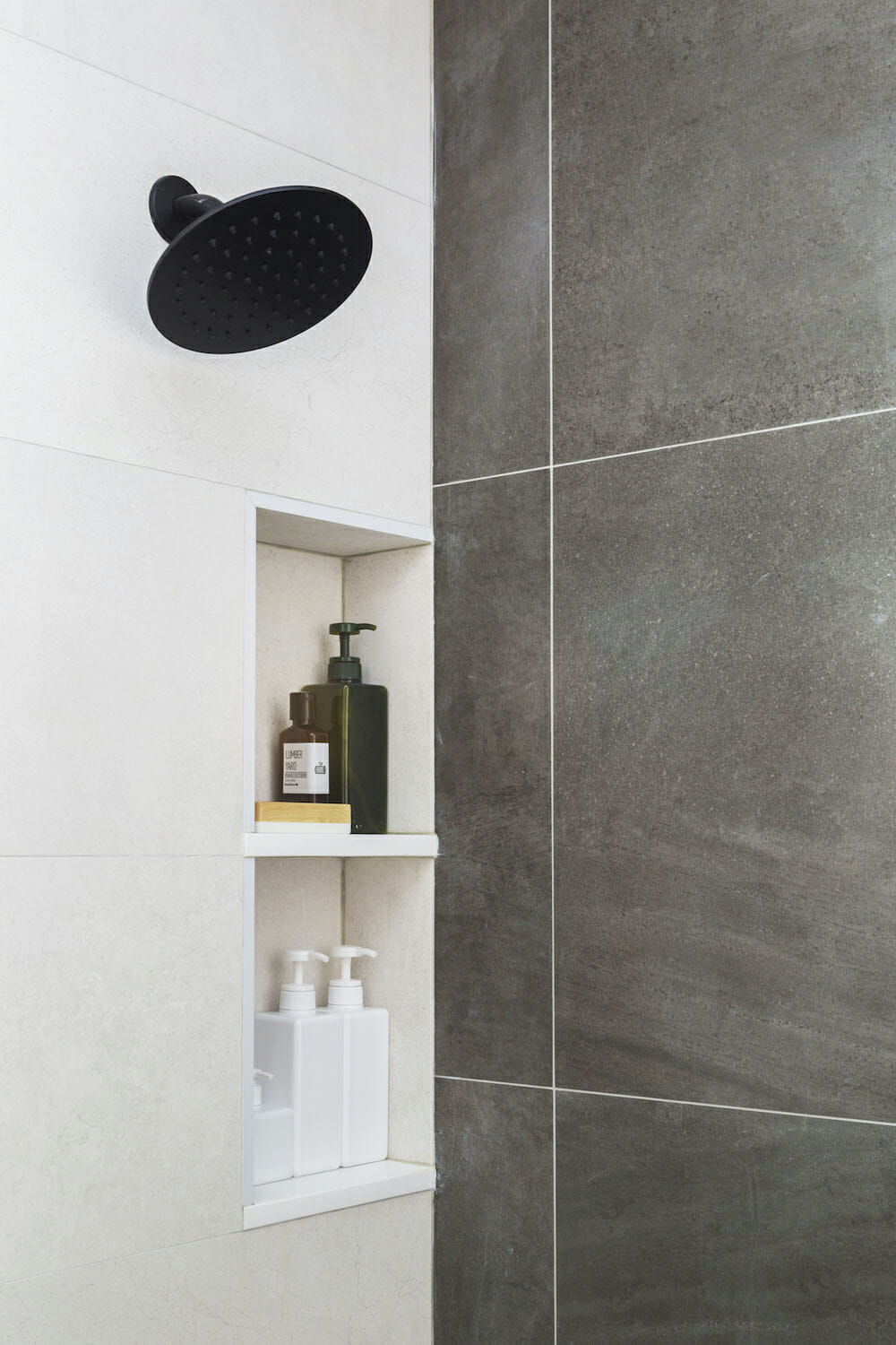 recessed shelves on off white wall and black shower head and dark gray tiles on adjacent wall after renovation