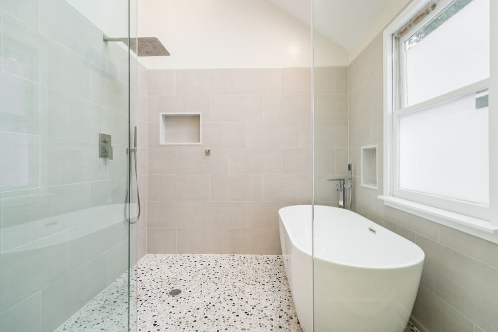 shower area with walk-in shower and bathtub and glass walls and recessed shelves and beige wall tiles and angled ceiling and large window after renovation