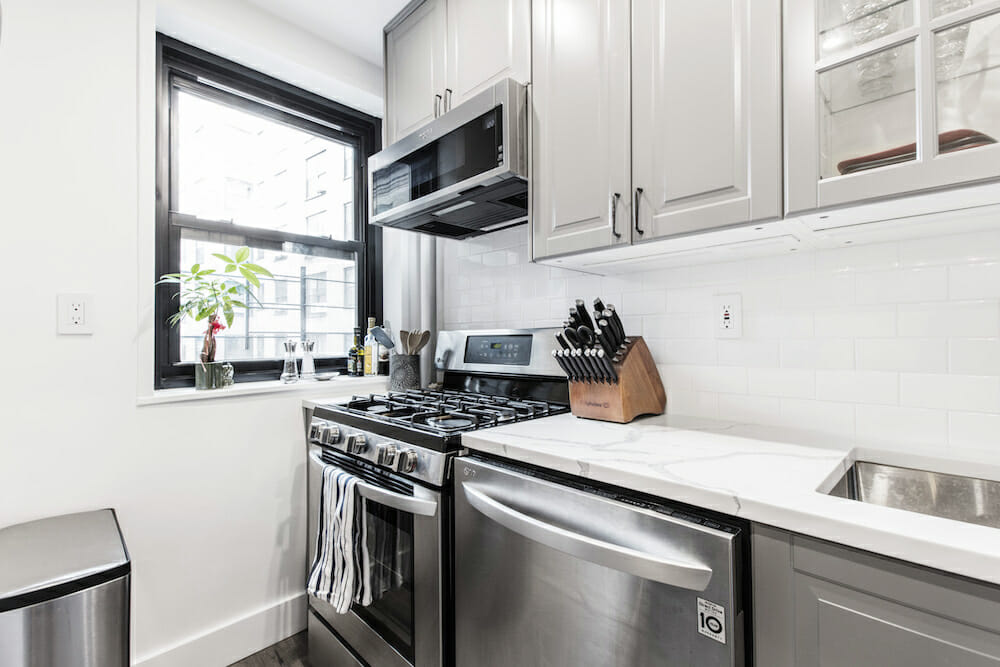 light gray kitchen cabinets and stainless steel appliances and white walls and window with black frame after renovation