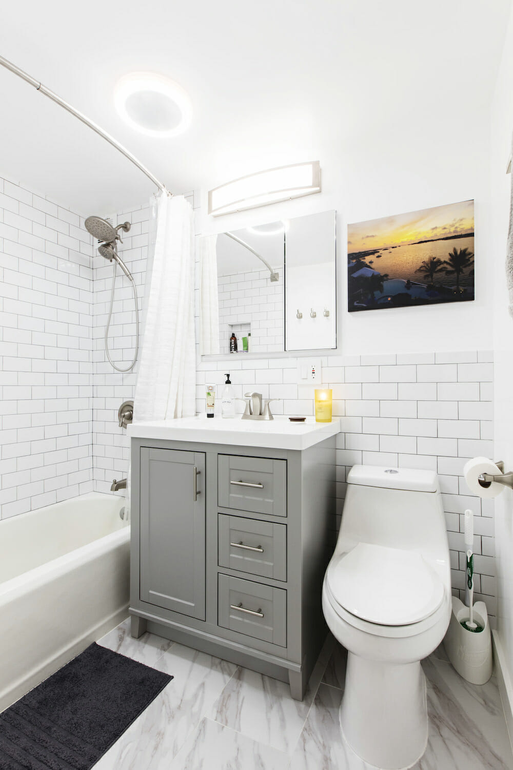 bathroom with white subway tiles on walls and bathtub and gray vanity with farmhouse sink and white marble tile flooring after renovation
