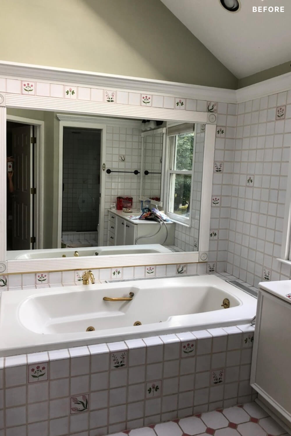 Patterned tiled white bathroom with white bathtub and large mirror before renovation
