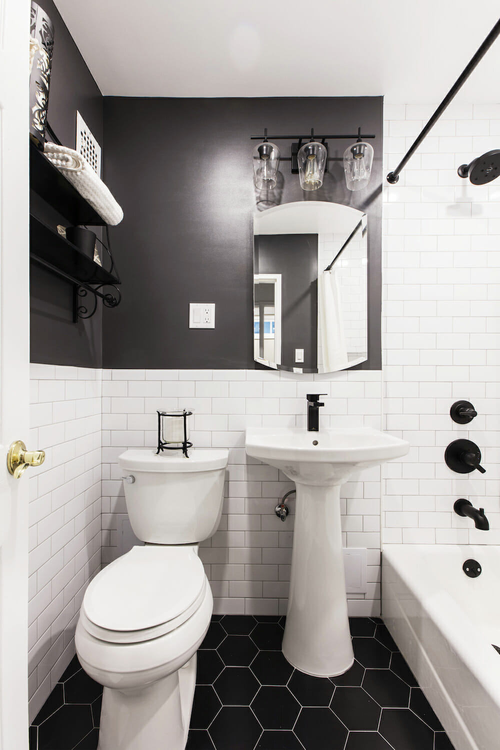 subway tiles on bathroom walls and pedastal sink and toilet and black half wall and black hexagon floor tiles and black faucets and fixtures after renovation
