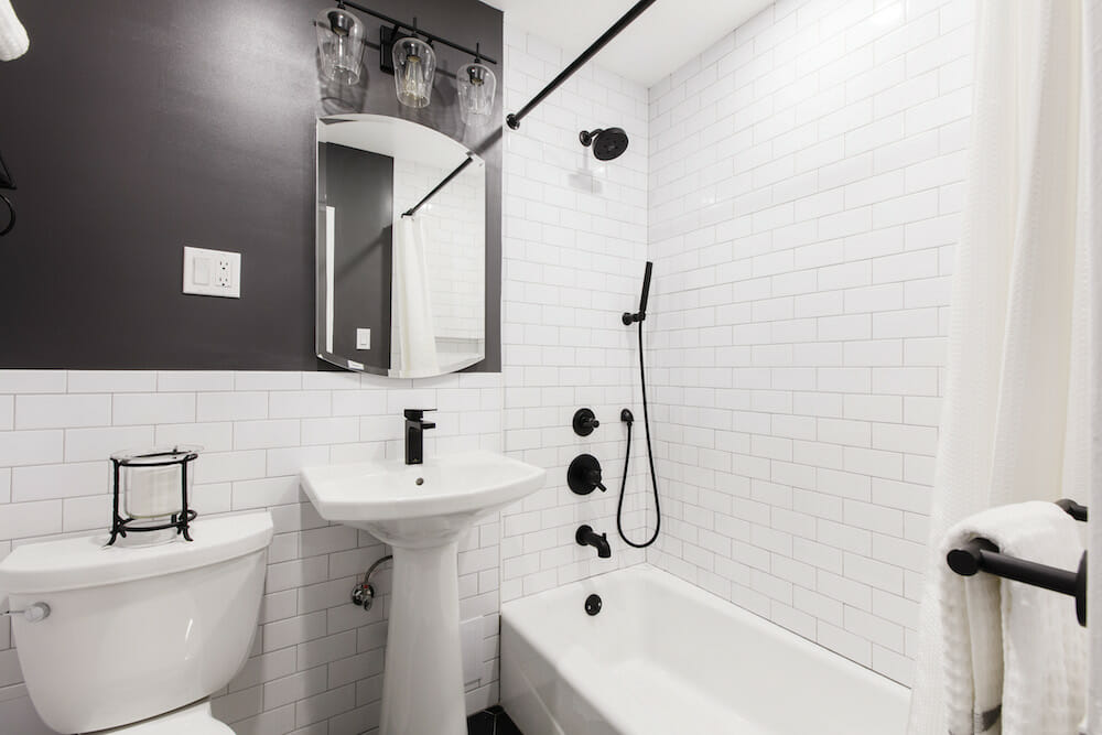 subway tiles on bathroom walls and pedastal sink and toilet and black half wall and bathtub with black shower head and fixtures after renovation