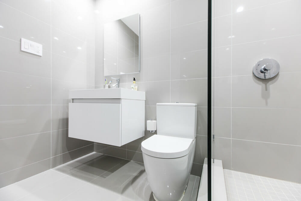 white floating bathroom vanity and toilet and walk-in shower with half glass wall and gray tiles on walls and floors after renovation