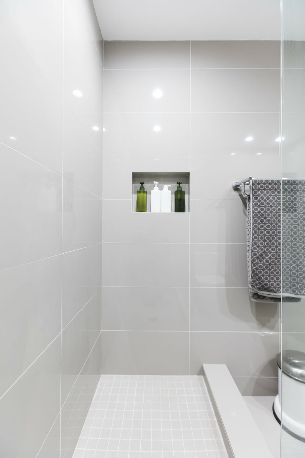 walk-in shower with half glass wall and small white tiles on floor and recessed shelf and light gray tiles on walls after renovation