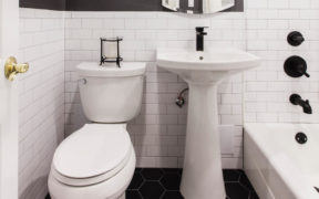 White bathroom with pedestal sink and white bathtub with black bathroom fitting after renovation