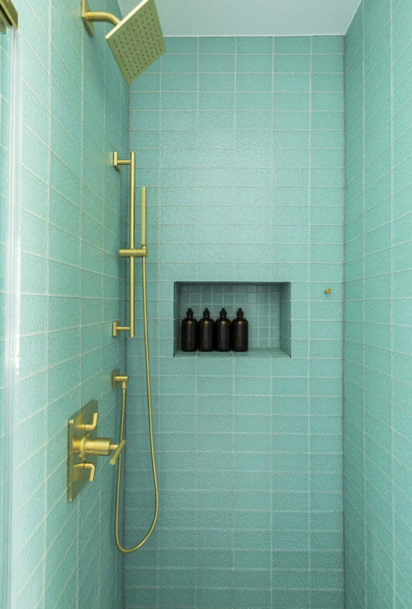 walk-in shower with recessed shelf and sea green tiles on wall and brushed gold shower head and fixtures after renovation