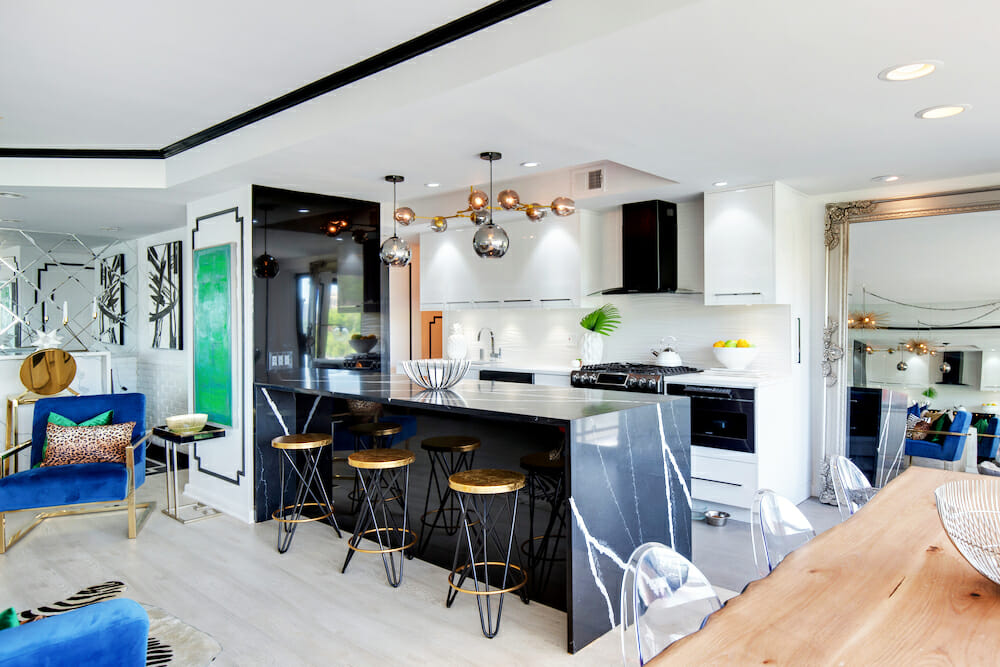 open kitchen with white cabinets and island with black marble countertop and pendant lights and tray ceiling in the dining area with black trim after renovation