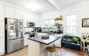 kitchen with hardwood floors and white cabinets and black countertop and stainless steel appliances and white walls and ceiling beam after renovation