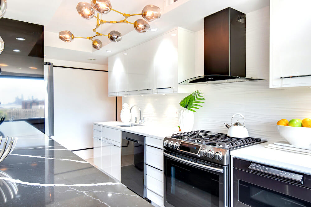 white kitchen cabinets with stainless steel appliances and white backsplash tile and contemporary chadelier after renovation