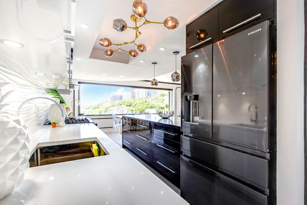 marble countertop in kitchen with undermount sink and dark gray stainless steel appliances and black pull out drawers in the island and contemporary chandelier after renovation