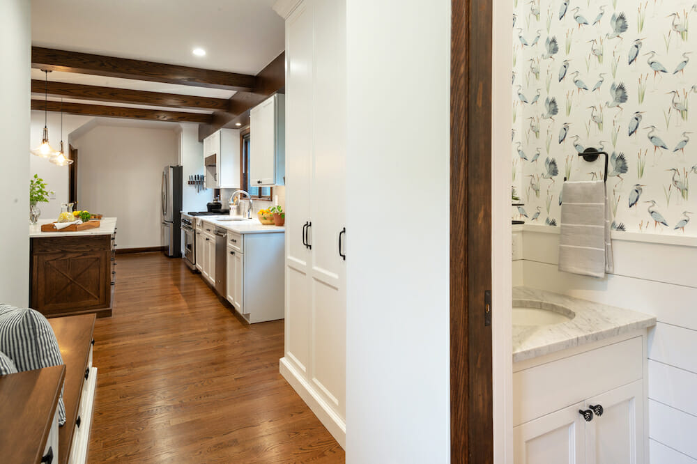 powder room and kitchen with white walls and hardwood floors and exposed wood beams in the kitchen after renovation